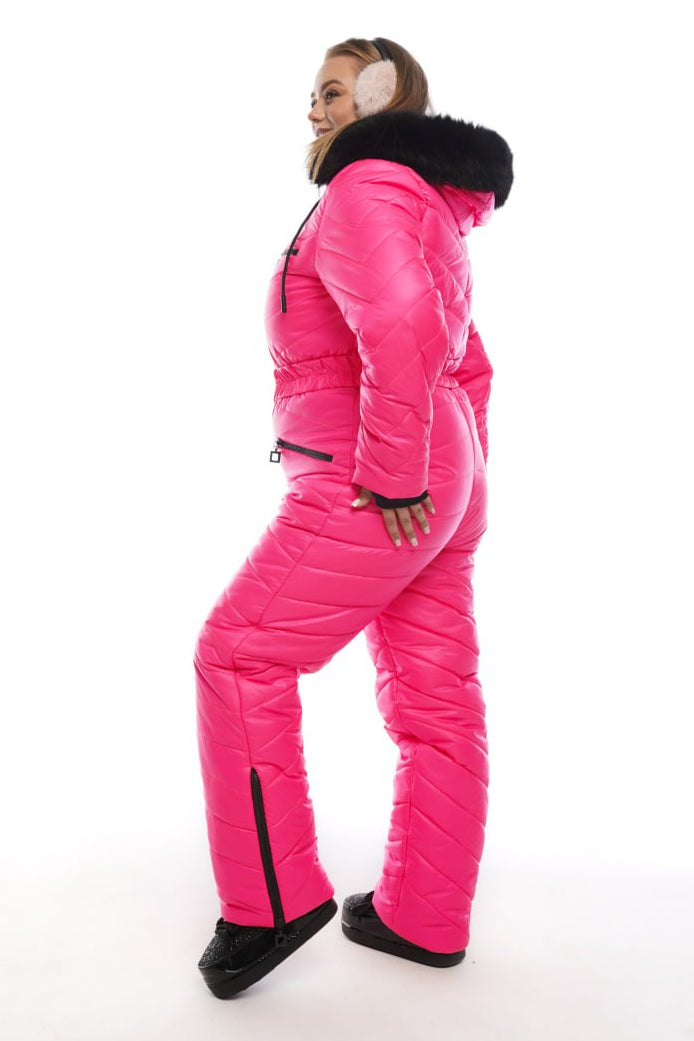 Person wearing a bright pink snowsuit with black fur trim on a white background